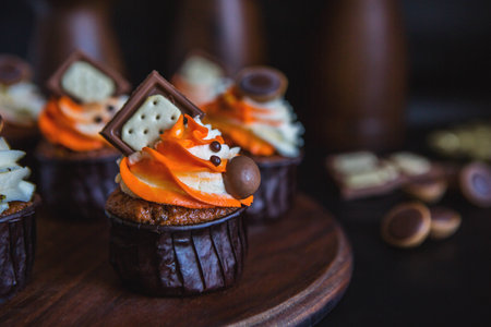Cupcakes with orange-and-white cream in a dark glass, decorated with chocolate, biscuits and sweets stand on a stand of dark wood on a dark backgroundの写真素材