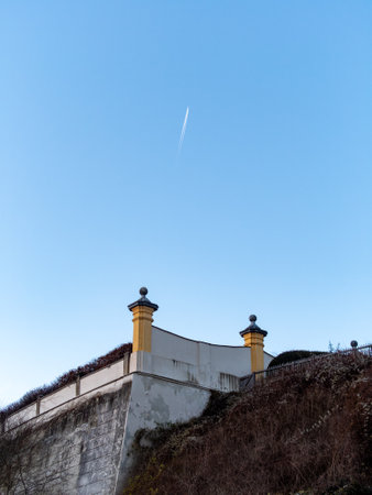 A historical wall with decorative pillars stands prominently against a vibrant blue sky. A swift vapor trail cuts through the serene atmosphere, hinting at distant travel.の写真素材