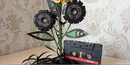 A unique sculpture made from old cassette tapes is displayed on a table. The tapes are creatively arranged to resemble flowers, showcasing artistic recycling in a modern indoor setting.の写真素材