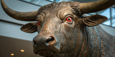 A large bronze bull sculpture with red eyes stands prominently in a contemporary art gallery. The artwork showcases intricate detailing and captures the attention of visitors nearby.の写真素材