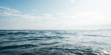 Gentle waves flow across the surface of the ocean, mirroring the expansive blue sky and soft clouds above in the serene backdrop of late afternoon.の写真素材