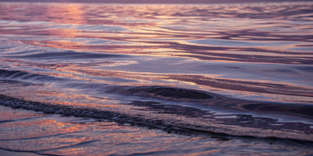 Soft waves lap at the shoreline as vibrant hues of sunset play across the water's surface, creating...