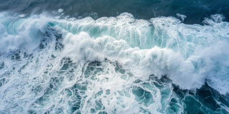 Turbulent blue waves crash against the rocky shoreline under clear skies, showcasing natureâs raw power in a coastal location during the daytime. The dynamic movement of water creates foam and spray.の写真素材