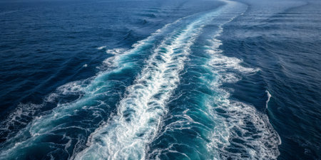 Bright blue ocean waters exhibit swirling patterns as a boat passes, leaving behind a wake that contrasts with the calm sea. The sun illuminates the scene vividly.の写真素材