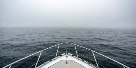 A boat glides smoothly over still waters shrouded in thick fog, creating an air of mystery. The journey takes place in the early morning, highlighting the tranquility of the moment.の写真素材