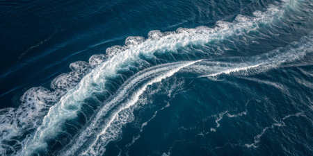 Bright sunlight reflects off the deep blue ocean, creating intricate patterns in the waves. The smooth movement demonstrates the power and beauty of the sea near the coastline.の写真素材