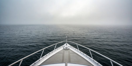 A yacht glides through calm waters as thick fog envelops the horizon, creating an atmosphere of...
