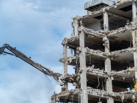 Concrete structures are being dismantled by heavy machinery in an urban setting under a clear sky....