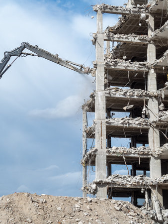 Heavy machinery operates at a construction site, tearing down a concrete structure under a clear...