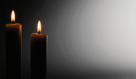 Two candles burn softly in a dim space, casting a warm glow. The flickering flames create shadows, enhancing the serene ambiance and inviting relaxation and reflection.の写真素材