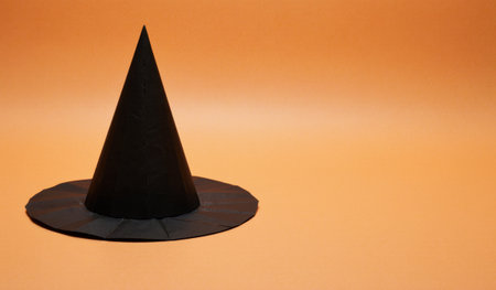 A tall black witch hat stands alone on a bright, warm orange background. Its simple design adds a touch of magic, perfect for Halloween celebrations or themed parties.の写真素材