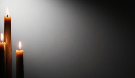 Three tall, narrow candles burn gently, casting a warm glow against a dark background. The flickering flames create a peaceful and inviting ambiance perfect for quiet moments.の写真素材