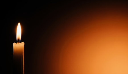 A solitary candle burns brightly in the dark, casting a warm glow against the shadows. This serene moment captures the essence of tranquility and reflection, inviting peace.の写真素材