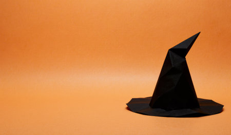 A black origami witch hat stands proudly on a bright orange backdrop, evoking a sense of mystery and the spirit of Halloween, inviting creativity and festive fun.の写真素材
