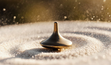 A brass spinning top glides effortlessly atop fine sand, creating swirling patterns as sunlight bathes the scene in warm hues. Its motion captures a moment of playful tranquility in nature.の写真素材