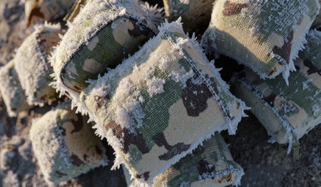 Camouflage fabric pieces covered in frost sit on a cold, snowy ground, showcasing their patterns in a chilly environment.の写真素材