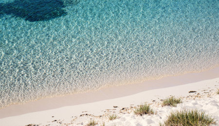 Soft waves meet the shoreline as the sun shines brightly on a quiet beach. Crystal-clear water...
