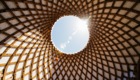Soft sunlight streams through a circular opening in a unique wooden dome. The intricate lattice design above creates a warm and inviting atmosphere, perfect for relaxation and reflection.の写真素材