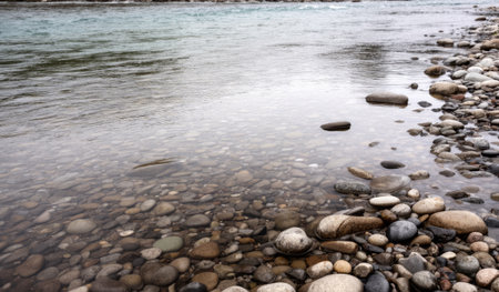 Calm waters reflect the soft morning light as smooth pebbles line the riverbank. The serene scene invites a moment of peace, surrounded by nature's beauty and gentle sounds of flowing water.の写真素材