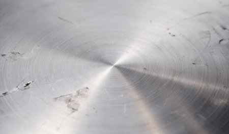 A close-up view reveals a smooth, shiny metal surface marked with scratches and patterns, illuminated by natural light in a workshop.の写真素材