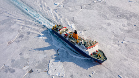 A ship cuts through ice in the Arctic ocean. It clears a path in the thick ice while sunlight reflects off the water. The boat works to keep the route open for research and travel.の写真素材
