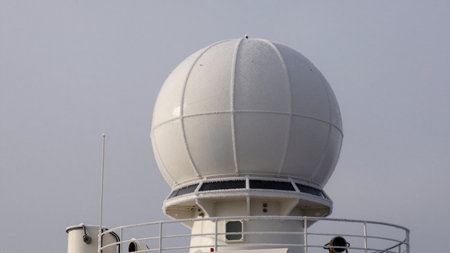 A radar dome sits atop a ship in the harbor. The structure is used for navigation and tracking. The sky is cloudy and the sea is still.の写真素材