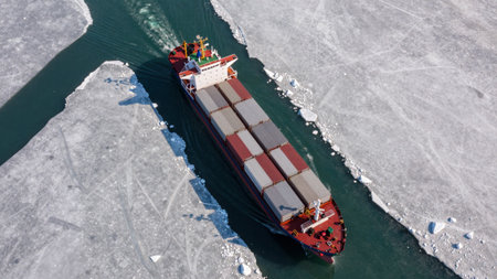 A cargo ship moves through narrow paths in icy water. Ice floats around the vessel as it travels. This scene is set in a remote area during winter.の写真素材