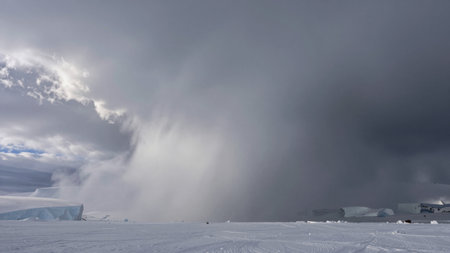 Dark clouds form over a vast snowy area in Antarctica. The scene shows the onset of a storm with low visibility and strong winds indicating a weather change.の写真素材