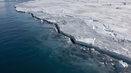 A large crack in the ice forms along the coast of a polar region. Water is visible below the broken...