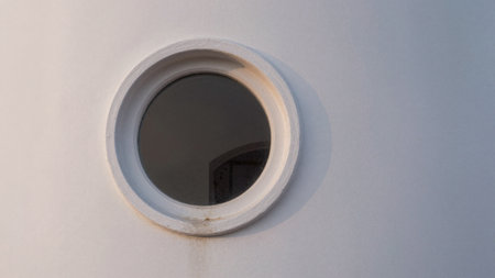 A small round window set into a clean white wall lets soft evening light filter through, casting...