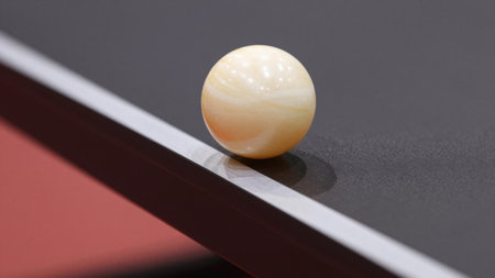 A table tennis ball rests delicately on the edge of a sleek black table, capturing the excitement and anticipation of the game. It symbolizes precision and skill in motion.の写真素材