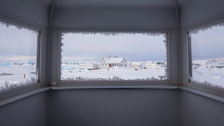 A cozy interior frames a picturesque view of a snow-covered village. The landscape is serene, with...