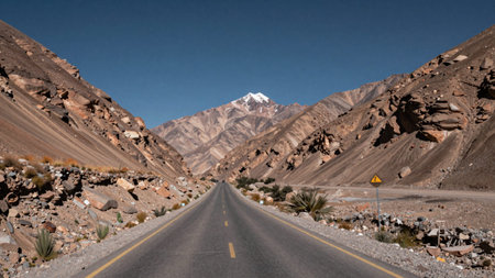 Captures a long, straight, asphalt road winding through a vast, barren landscape, the road is...