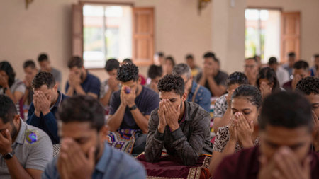 Group of people, mostly men and women, sitting in a church, all with their hands covering their...