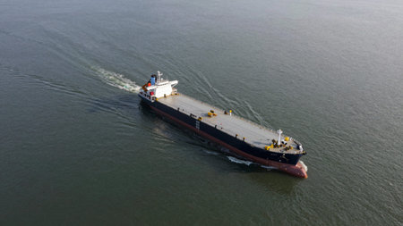 Cargo ship sailing on a calm, overcast sea, the ship is predominantly dark blue with a maroon stripe...