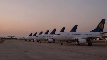 Of airplanes parked on a tarmac at an airport during sunset. The sky is a gradient of soft pink and...