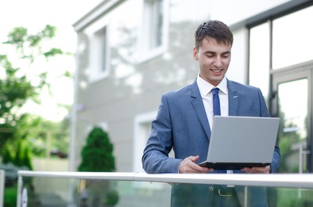 Smiling businessman with his laptop next to the office buildingの写真素材