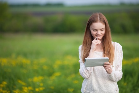Happy Girl European appearance standing on the grass with notebook and penの写真素材