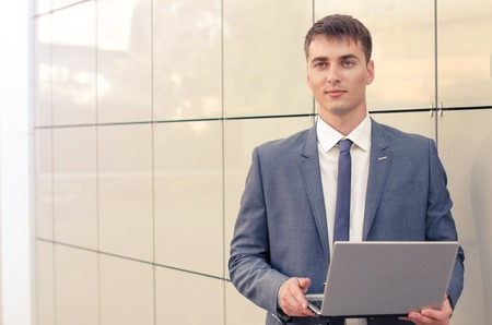 Smiling businessman with his laptop next to the office buildingの写真素材