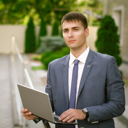 Smiling businessman with his laptop next to the office buildingの写真素材
