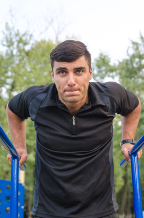 fitness, sport, exercising, training and lifestyle concept - young man doing triceps dip on parallel...