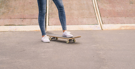 Close up of fit lady in white sneakers ready to extreme ride her skateboard in sunlight. Modern...