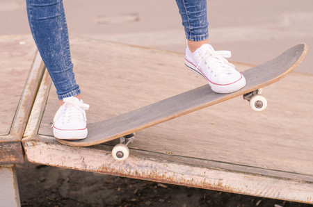 Close up of fit lady in white sneakers ready to extreme ride her skateboard in sunlight. Modern...