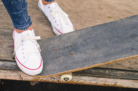 Close up of fit lady in white sneakers ready to extreme ride her skateboard in sunlight. Modern urban hipster girl having fun. Good sunny summer day for skateboarding and having fun.の写真素材