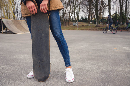 Portrait of of a young happy girl holding a skateboard. Skate park cyclist in the backgroundの写真素材