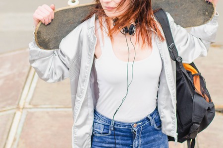 Portrait of of a young happy girl holding a skateboard. Skate park in the backgroundの写真素材