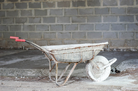 old dirty metallic wheelbarrow on the house during building backgroundの写真素材