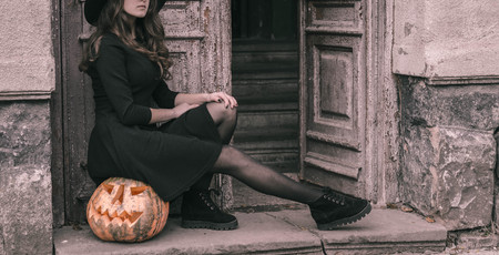 Happy creepy gothic young woman in witch halloween costume with halloween pumpkin.の写真素材