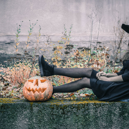 Happy creepy unrecognizible gothic young woman in witch halloween costume with halloween pumpkin.の写真素材