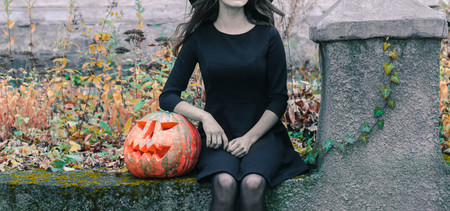 Happy creepy unrecognizible gothic young woman in witch halloween costume with halloween pumpkin.の写真素材